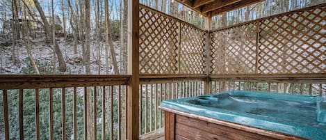 A wooden deck with a hot tub and a bench, surrounded by a lattice fence.