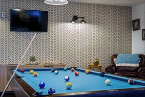 A pool table with balls, a television mounted on the wall, and a patterned wallpaper. - Locklyn's Loft Views, Hot Tub, Game Room & MORE! (Gatlinburg)