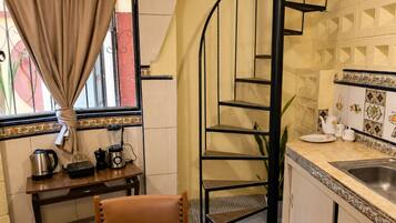 Una cocina con una escalera de caracol, una mesa de comedor con sillas, un ventanal con cortinas y un lavabo con azulejos decorativos.