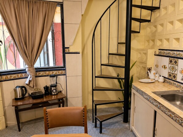 Una cocina con una escalera de caracol, una mesa de comedor con sillas, un ventanal con cortinas y un lavabo con azulejos decorativos.