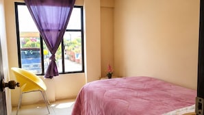 Un dormitorio con una cama, una silla, un ventanal con cortinas, una lámpara de araña y vistas al exterior.