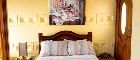 Un dormitorio con cama de madera, un cuadro en la pared, una puerta de madera y suelo con estampado.