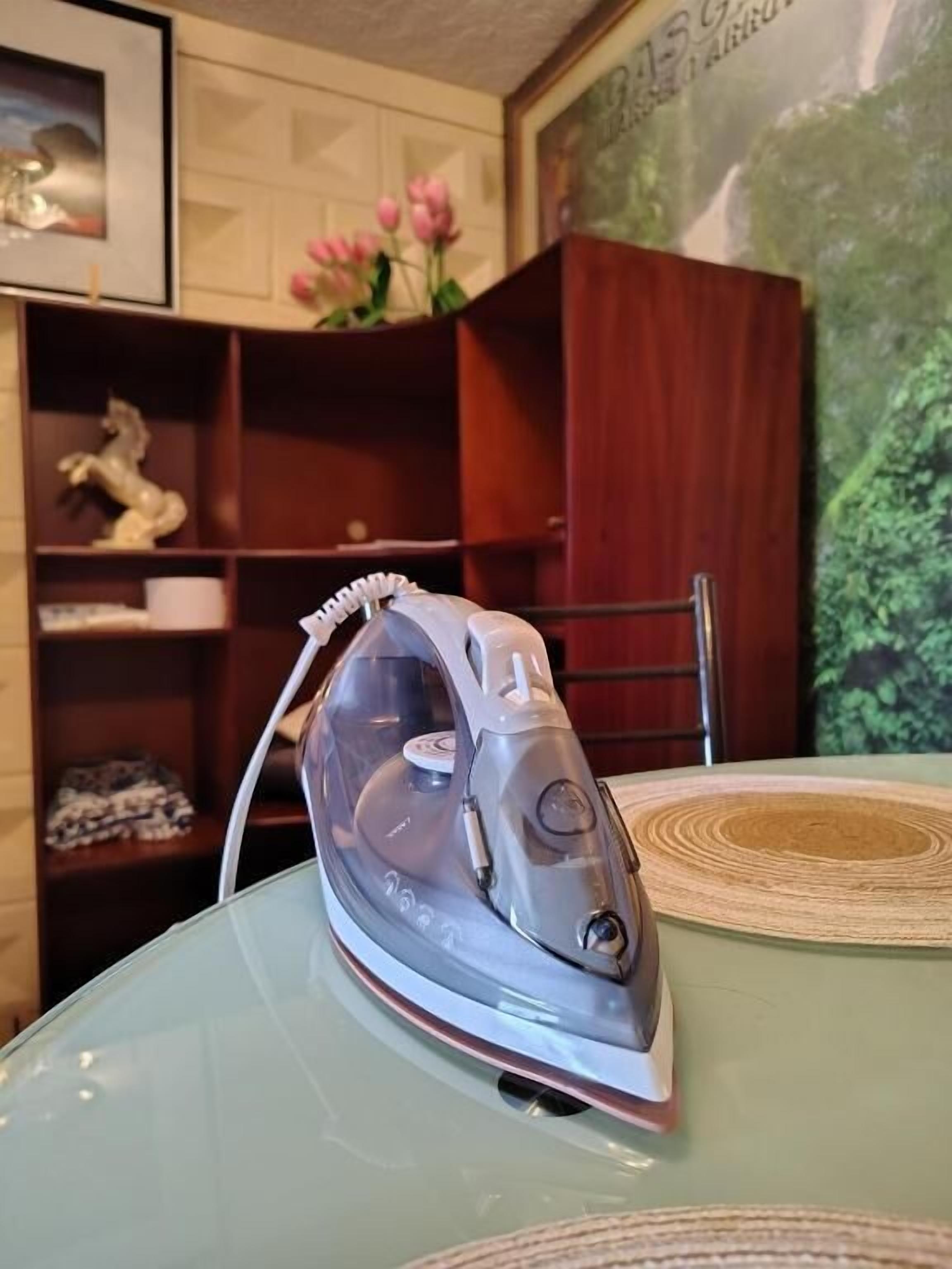 A table with a clear glass top and a modern electric iron placed on it.