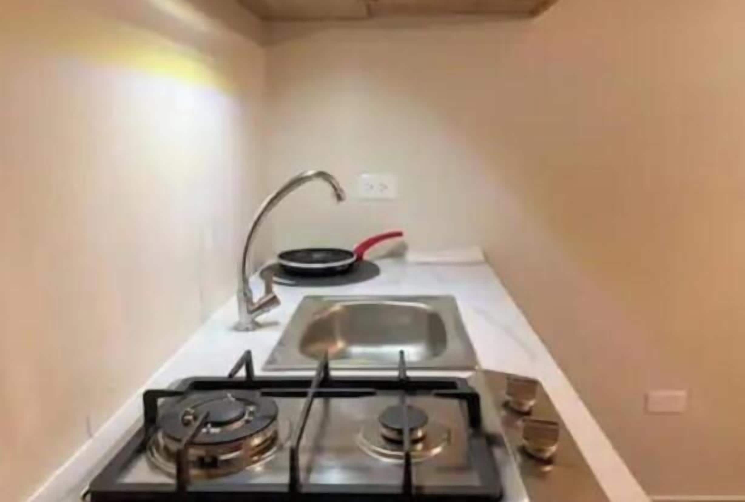 Cozinha compacta com fogão a gás, pia e frigideira vermelha.