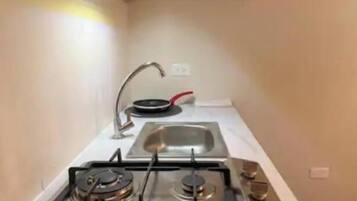 Cozinha compacta com fogão a gás, pia e frigideira vermelha.