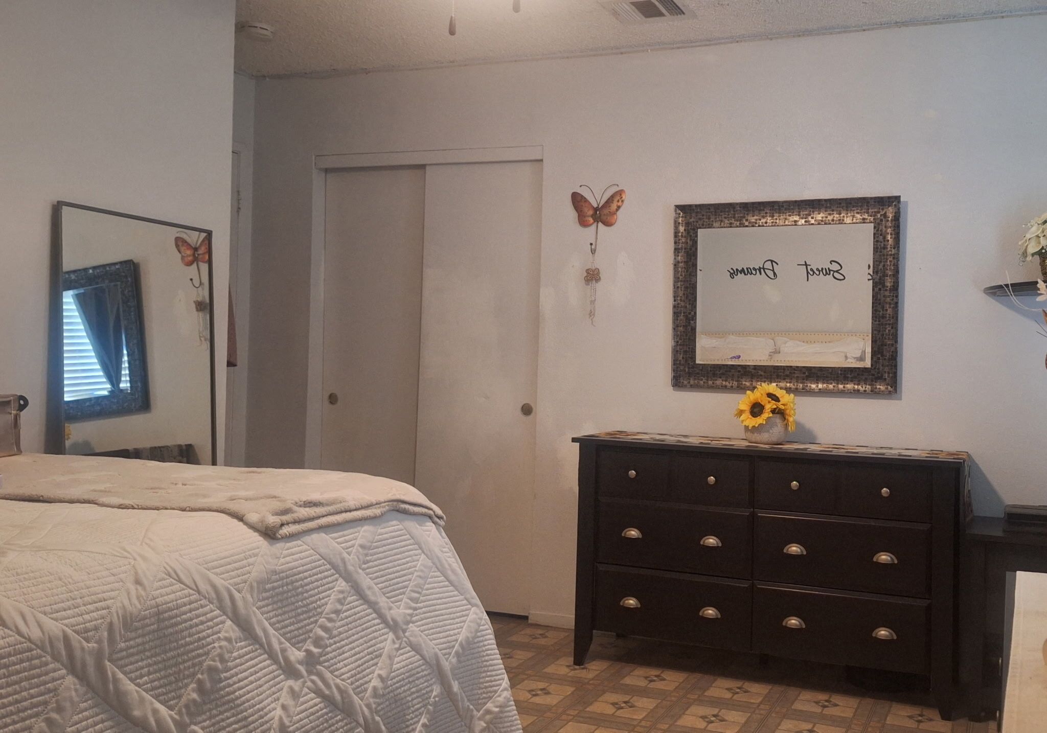 A bedroom with a bed, dresser, mirror, and wall decorations including a framed certificate.