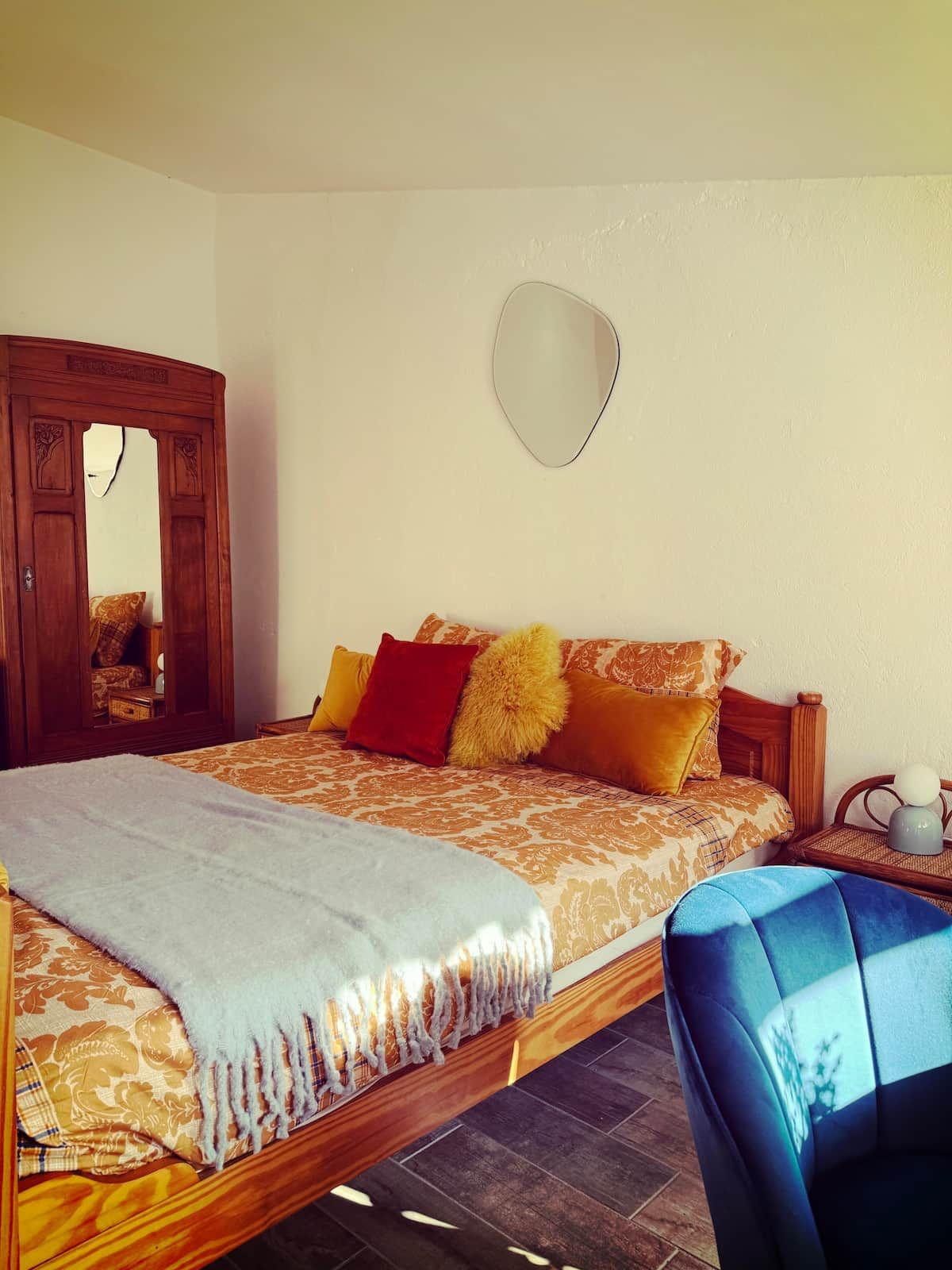 Quarto com cama, espelho, cadeira e mesa de cabeceira.
