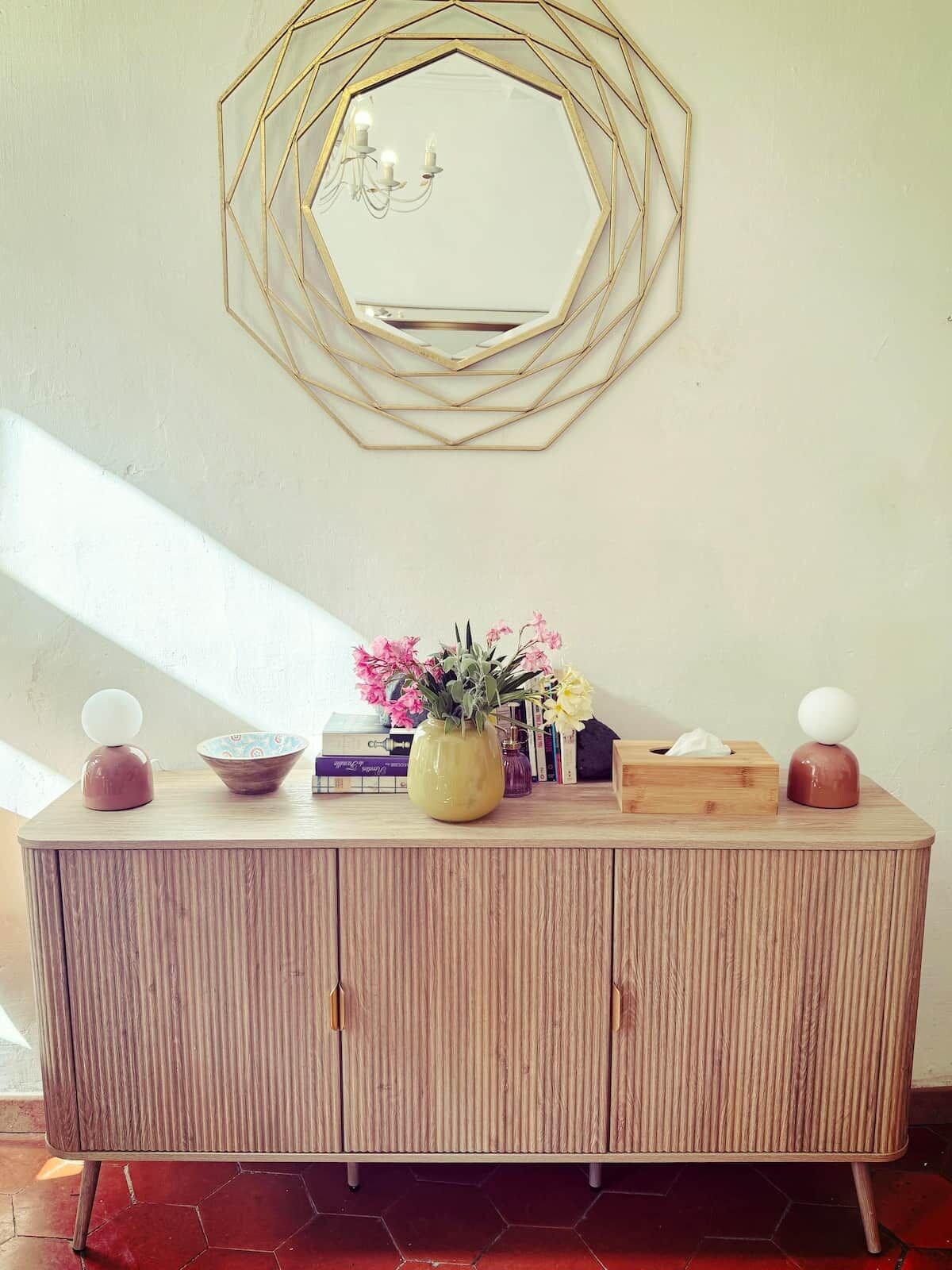 A wooden cabinet with a mirror above it, a vase with flowers, and a tissue box.