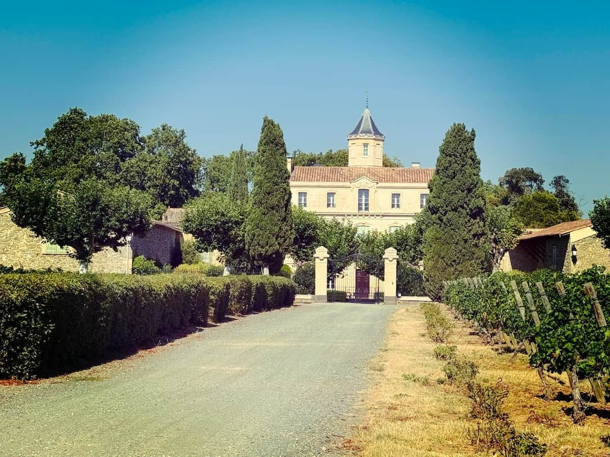 A large, historic building with a prominent tower, surrounded by well-maintained gardens and vineyards.