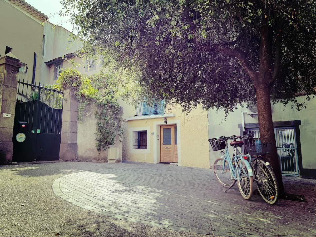A paved courtyard with a bicycle parked by a tree, a building entrance, and a gate.