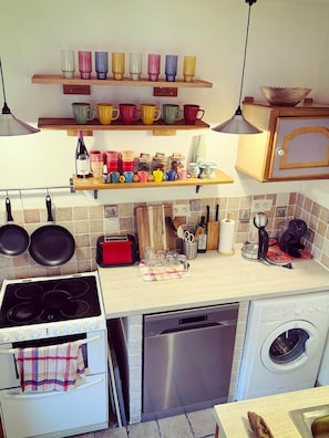 A kitchen with a stove, oven, dishwasher, and a variety of colorful mugs on shelves. - Charming Historic Townhouse with Private Terrace in Old Agde (Agde)