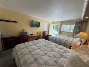 Habitación de hotel con dos camas, un escritorio con televisor, una silla y una ventana con cortinas.