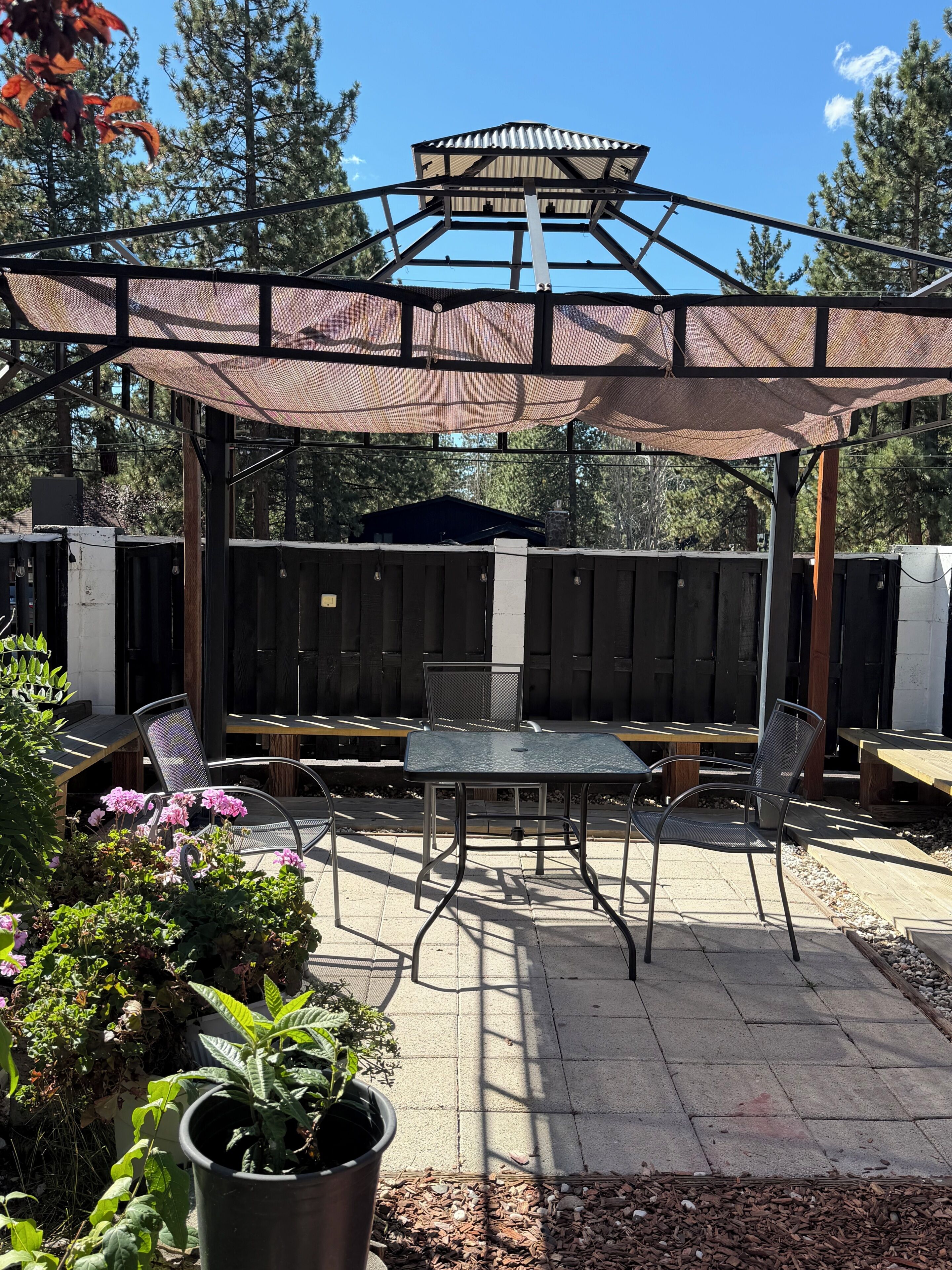 Een terras buiten met een overdekte zithoek, een tafel en stoelen.