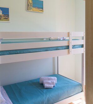 A bunk bed with a lower bunk and a top bunk, both with blue bedding. There is a painting on the wall above the bed. - LOBEA BEACH HOUSE - Enjoy a beach lifestyle! (Carini)