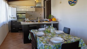 Zona pranzo con tavolo apparecchiato per quattro, cucina sullo sfondo e ventilatore a soffitto.