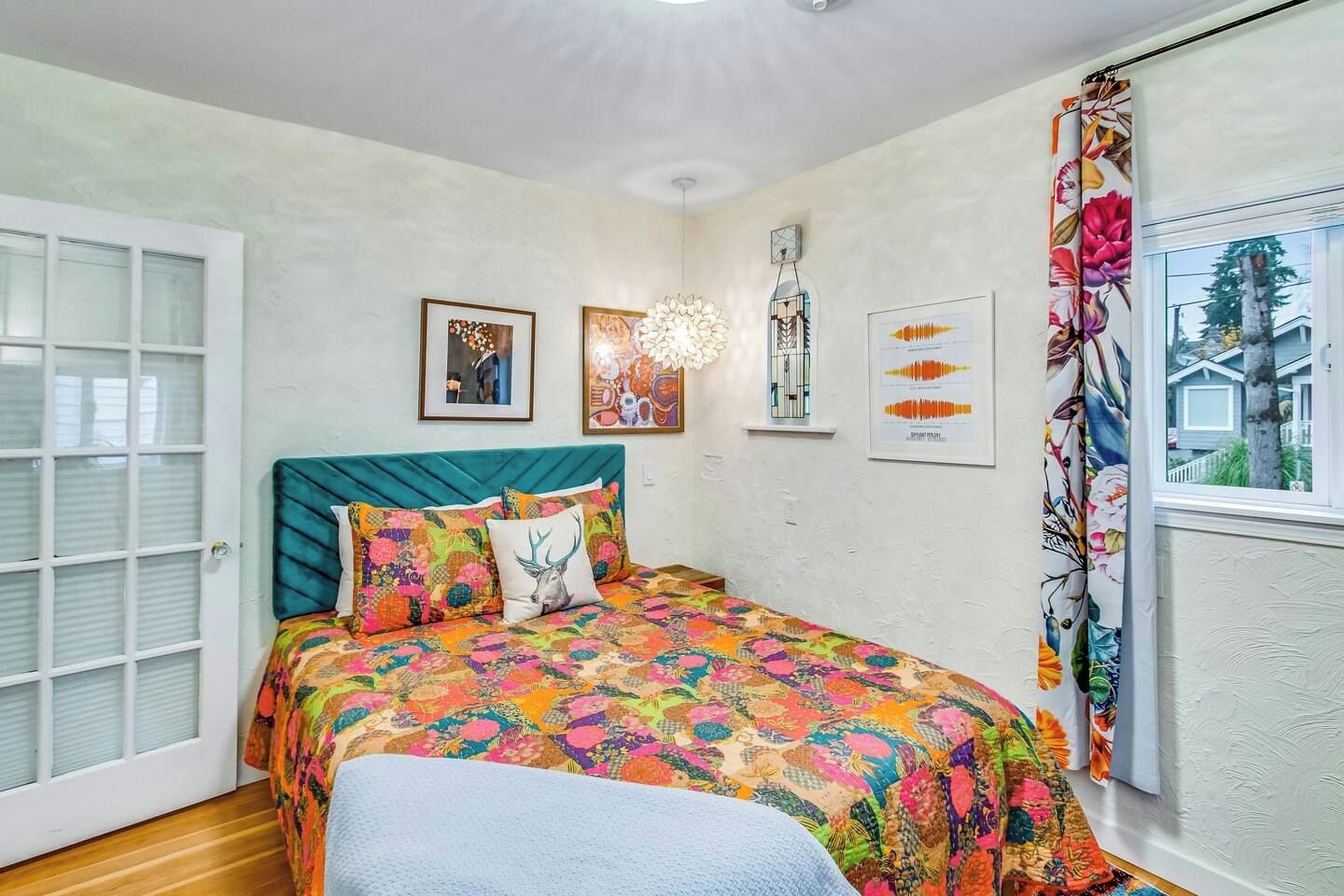Ein Schlafzimmer mit Bett, einem Fenster mit Vorhängen und Wandbildern.