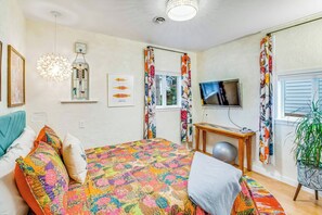 A bedroom with a large bed, a television, a plant, and a window with curtains. - Boho-Chic Seattle Home | Walk to Gas Works & More (Seattle)