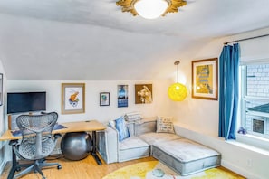 A modern living room with a sofa, a desk with a computer, exercise equipment, and artwork on the walls. - Boho-Chic Seattle Home | Walk to Gas Works & More (Seattle)