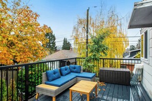 A deck with outdoor furniture, a view of autumn trees, and a building in the background. - Boho-Chic Seattle Home | Walk to Gas Works & More (Seattle)