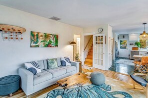 Ein modernes Wohnzimmer mit einem grauen Sofa, einem Couchtisch und einem Teppich. Eine Treppe führt in einen anderen Raum.