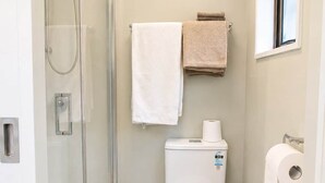 Ein kleines Badezimmer mit einer Duschkabine aus Glas, einer Toilette, einer grünen Matte und einem Handtuchhalter mit zwei Handtüchern.