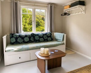 Habitació acollidora amb finestra, un sofà, una taula petita amb espelmes i una estant amb objectes.