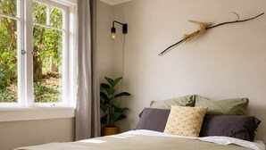 Ein Schlafzimmer mit einem Bett, einem Fenster, einer Pflanze und einer Wandleuchte.