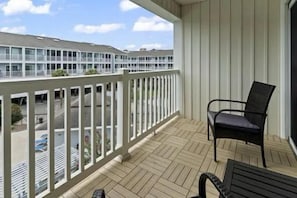 A balcony with a white railing, a black chair, and a wooden floor. - A Place at the Beach V (Horry County)