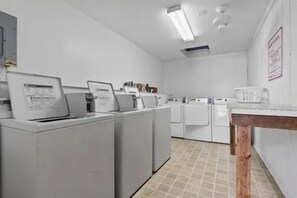A laundry room with multiple washing machines and dryers, a wooden table, and a tiled floor. - A Place at the Beach V (Horry County)