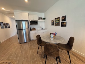 A compact kitchen with white cabinets, a stainless steel refrigerator, a microwave, and a sink. There is a round dining table with four chairs. - Private 1BR Apartment with Living Room, Washer & Dryer (Visalia)