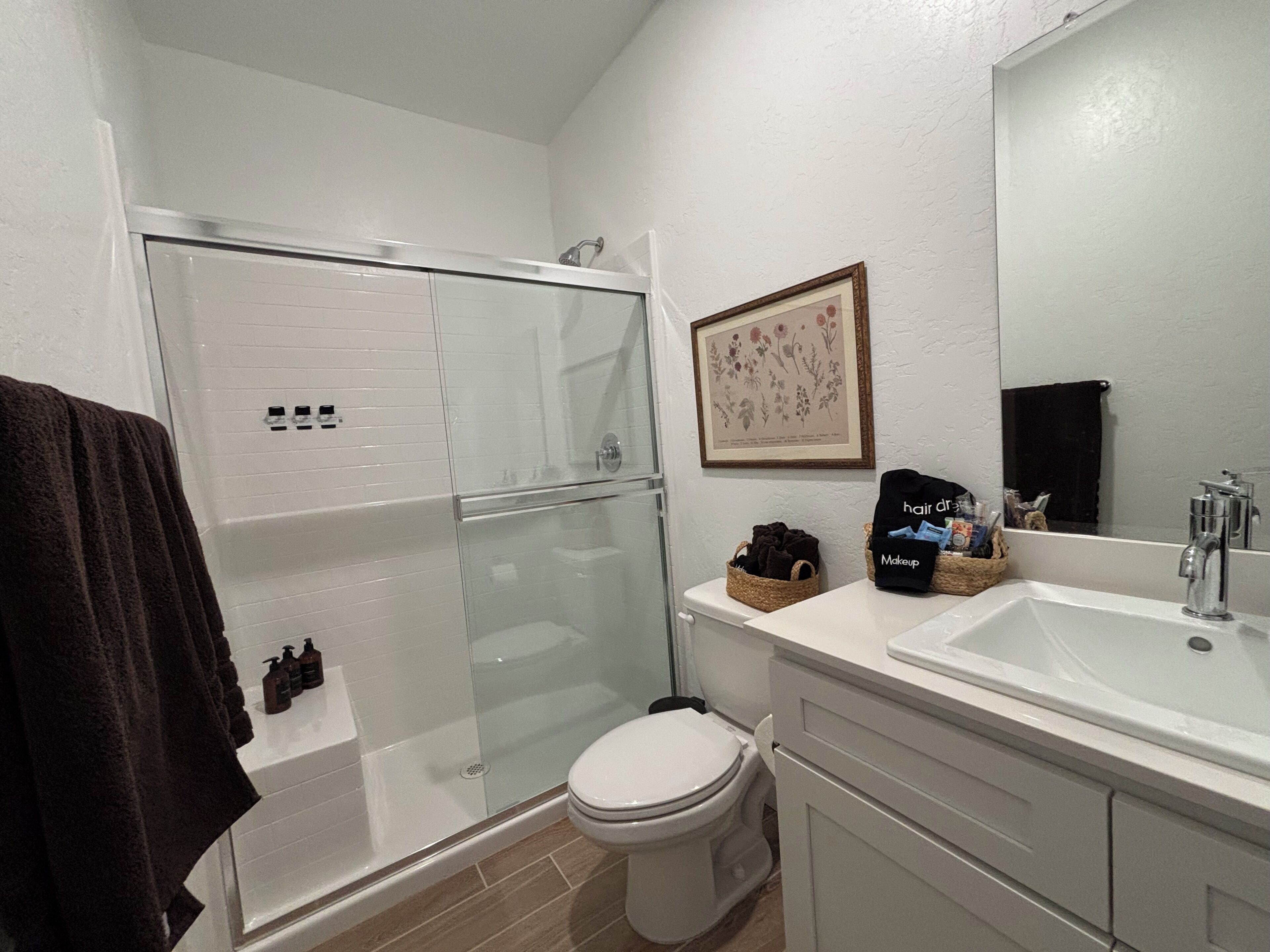 Une salle de bain dotée d’une douche à parois de verre, de toilettes, d’un lavabo avec un miroir et d’une estampe botanique encadrée au mur.