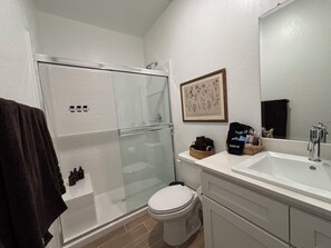 A bathroom with a glass-enclosed shower, a toilet, a sink with a mirror, and a framed botanical print on the wall. - Private 1BR Apartment with Living Room, Washer & Dryer (Visalia)
