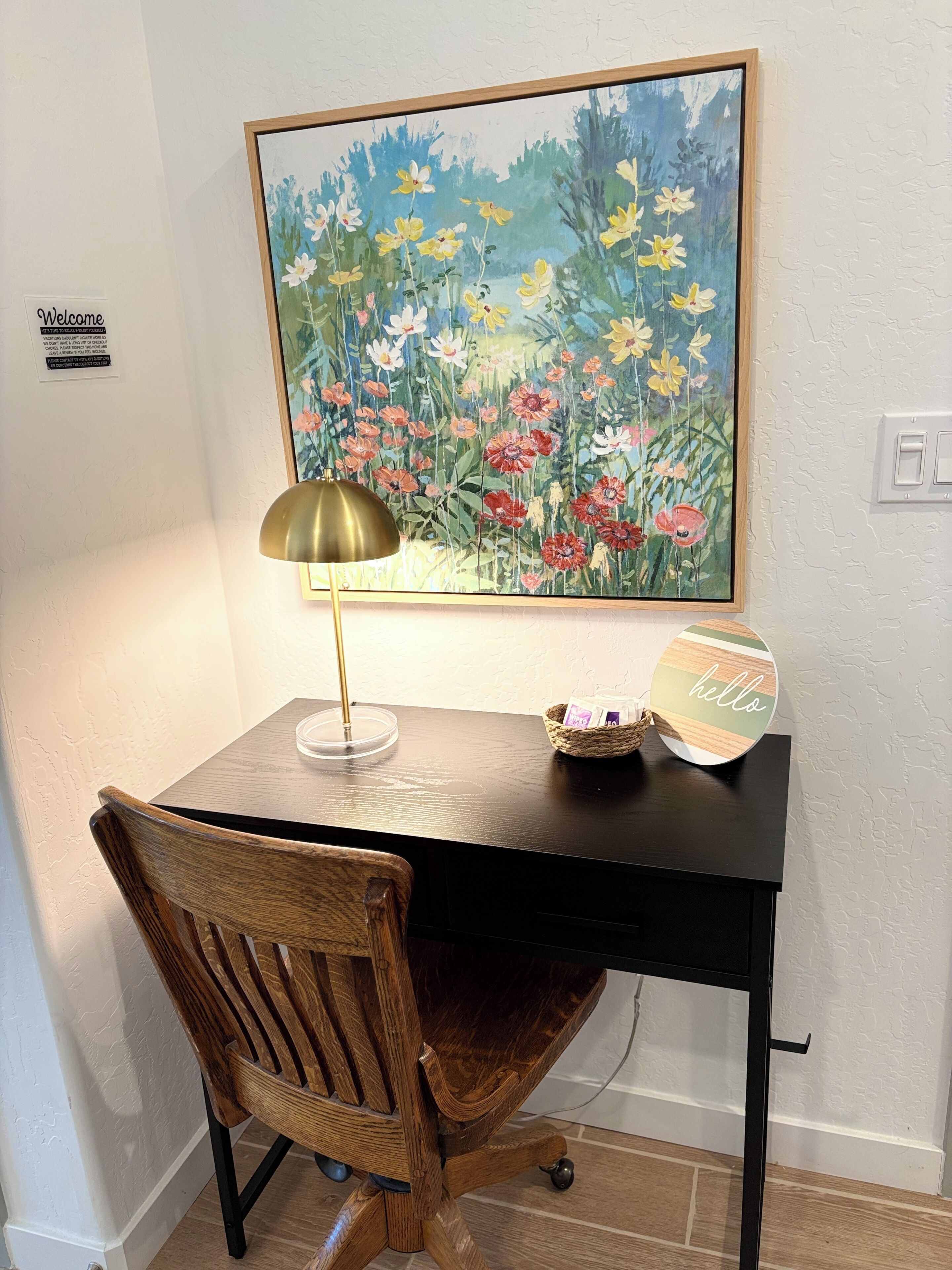 Uma mesa de madeira com uma luminária, uma cesta e uma placa com a palavra 'hello'.
