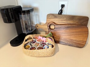 A coffee maker, a blender, a wooden cutting board, and a basket of coffee pods on a countertop. - Private 1BR Apartment with Living Room, Washer & Dryer (Visalia)