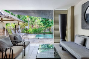 A modern living room with a glass coffee table, a sofa, and a chair. There is a pool visible through the glass. - Temple Escape 3 Bed Apartment with Private Pool (Craiglie)