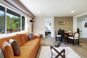 A modern living room with a sofa, a dining table, and chairs. There is a window providing a view of the outdoors. - Modern Duplex Unit w/ Backyard, Near Transit (Seattle)
