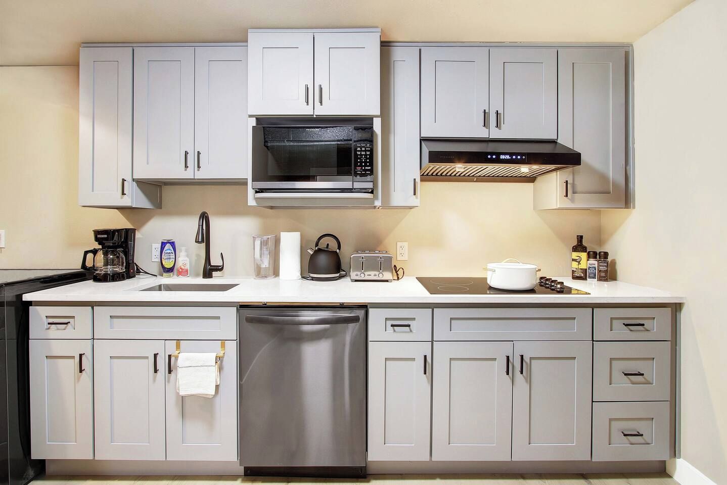A modern kitchen with grey cabinets, a stainless steel dishwasher, a microwave, a toaster, and a coffee maker.