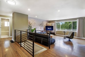 A modern living room with a flat-screen TV, a sofa, and a window with a view of trees. - Modern Seattle Duplex, Balcony w/ Serene View (Seattle)