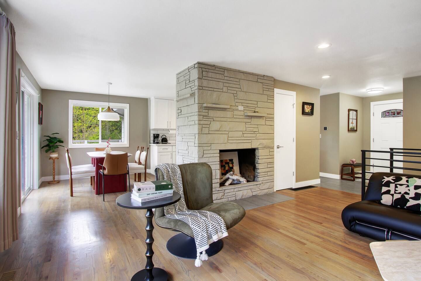 A living room with a stone fireplace, a dining area with a table and chairs, and a black leather sofa.