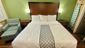 A hotel room with a bed, two bedside tables, a chair, and a wall-mounted ironing board. - Premium King Suite 106–Stroll Historic Downtown Great Restaurants & Unique Shops (Grants Pass)