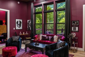 A modern living room with a red sofa, a coffee table, and a large window with a view of trees. - Adults-Only Couples Retreat · Private Hot Tub (Sevierville)
