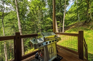 Ein Grill auf einer Holzterrasse mit Blick auf einen Wald.