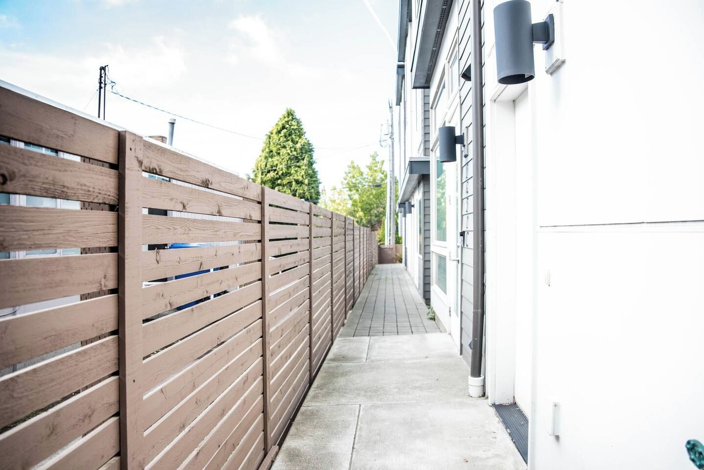 A narrow pathway flanked by a wooden fence and a building with a white exterior.