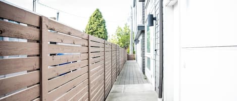 A narrow pathway flanked by a wooden fence and a building with a white exterior.