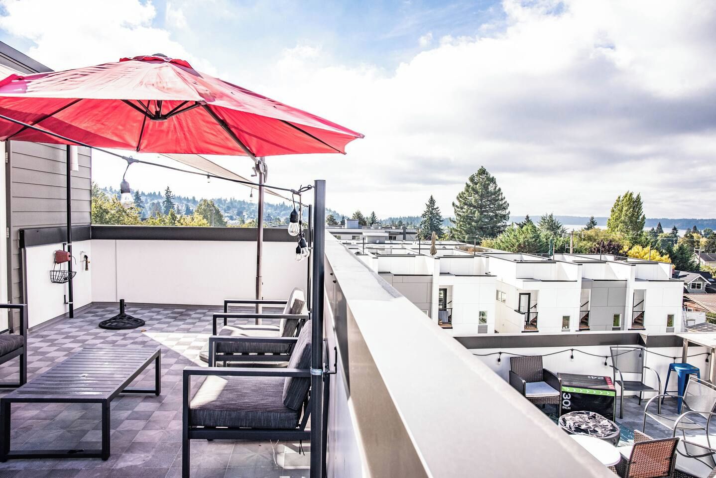 A balcony with a red umbrella, outdoor furniture, and a view of buildings and trees.
