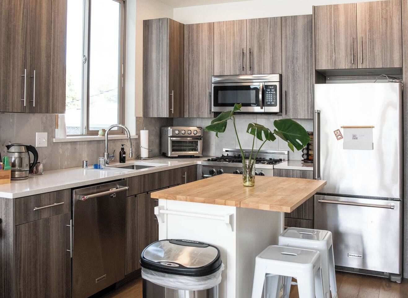 Une cuisine moderne avec des meubles en bois, des appareils en acier inoxydable, un îlot central en bois et un évier.