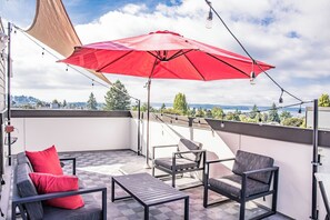 Eine Dachterrasse mit einem roten Sonnenschirm, Gartenmöbeln und Blick auf die Stadt.
