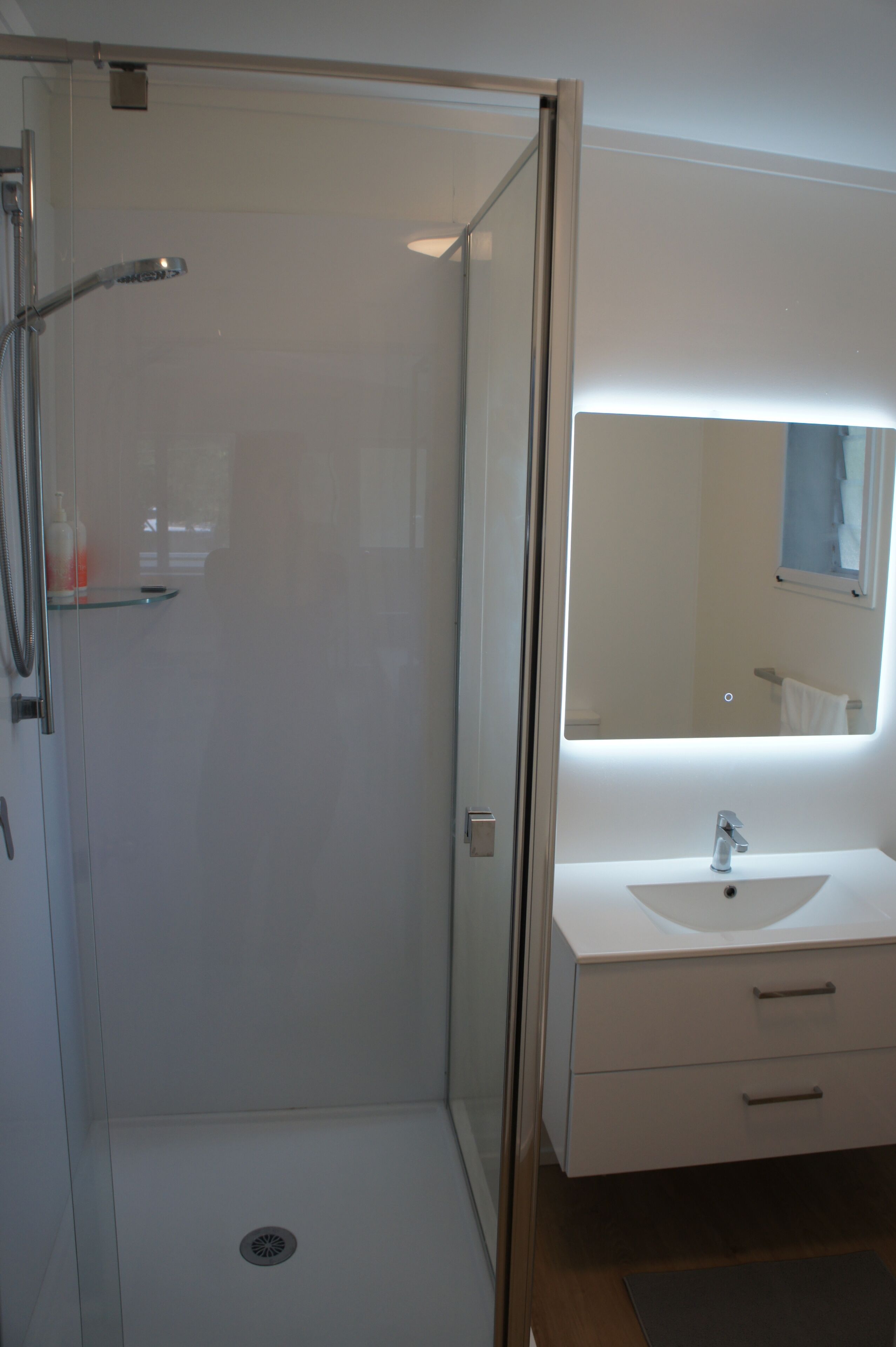 Un baño moderno con ducha envuelta en vidrio, un lavamanos blanco y un espejo grande.