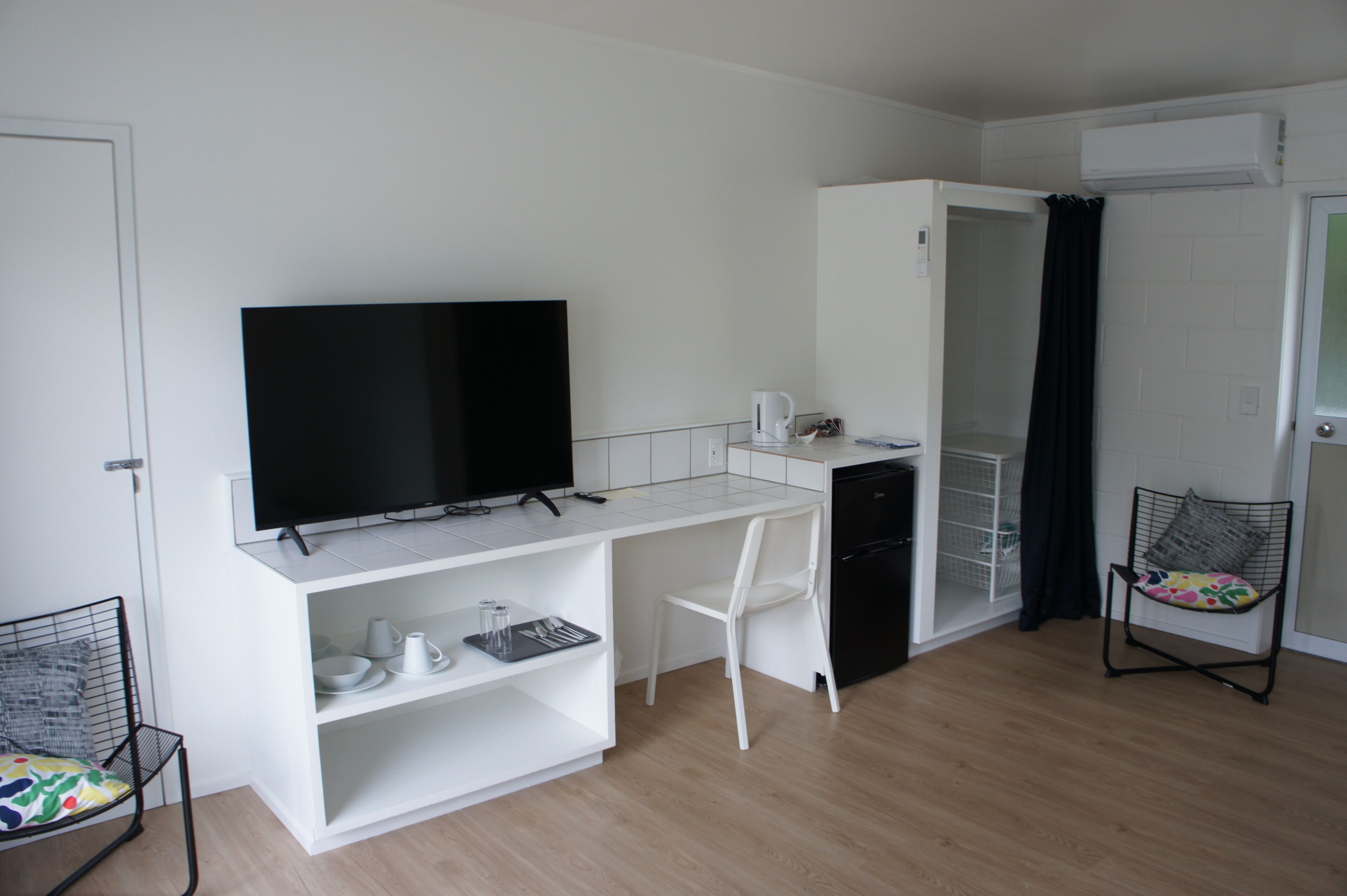 A compact kitchenette with a flat-screen TV, a white chair, and a small refrigerator.