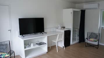 A compact kitchenette with a flat-screen TV, a white chair, and a small refrigerator.
